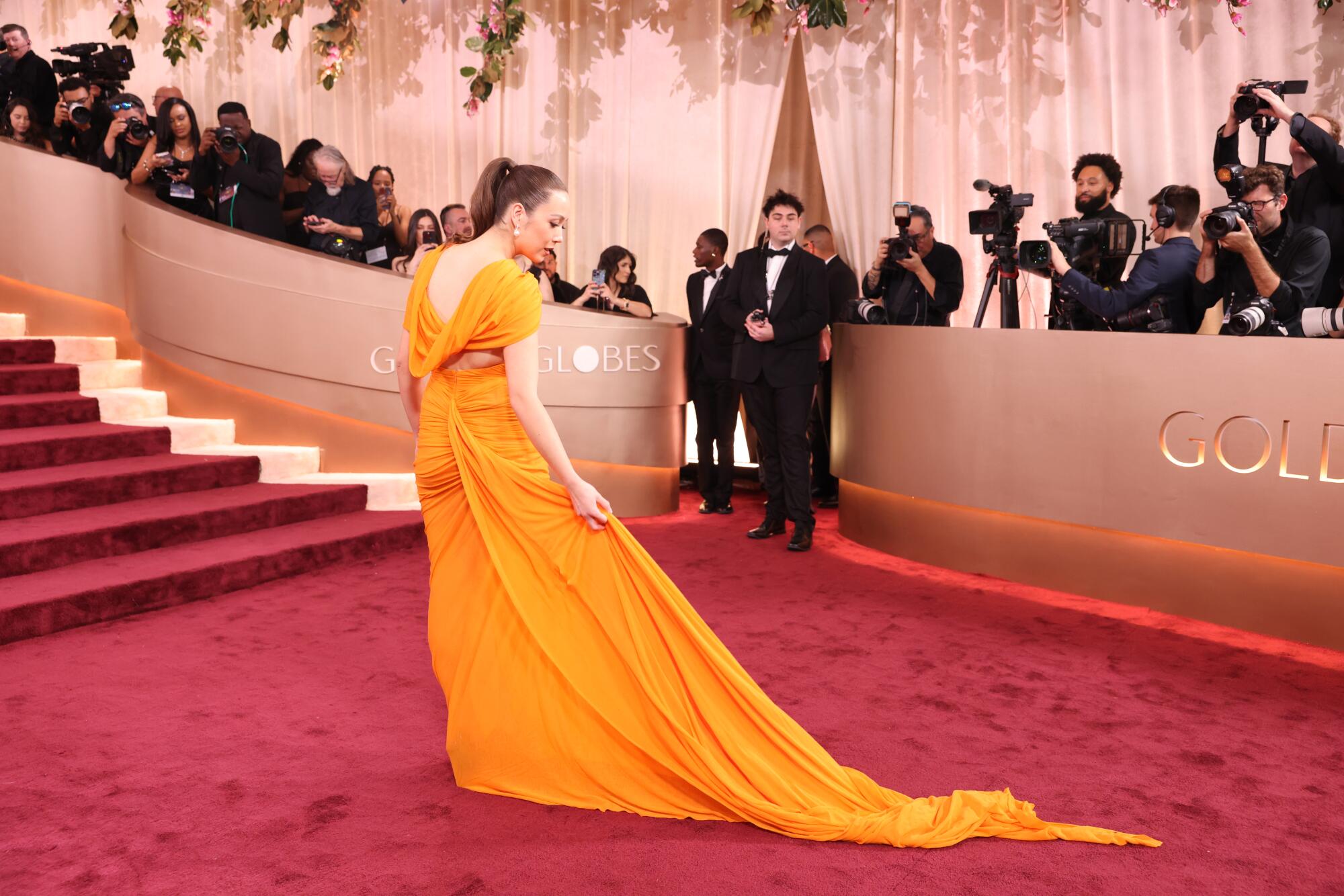 Laufey adjusts her orange gown's long train on the red carpet. 