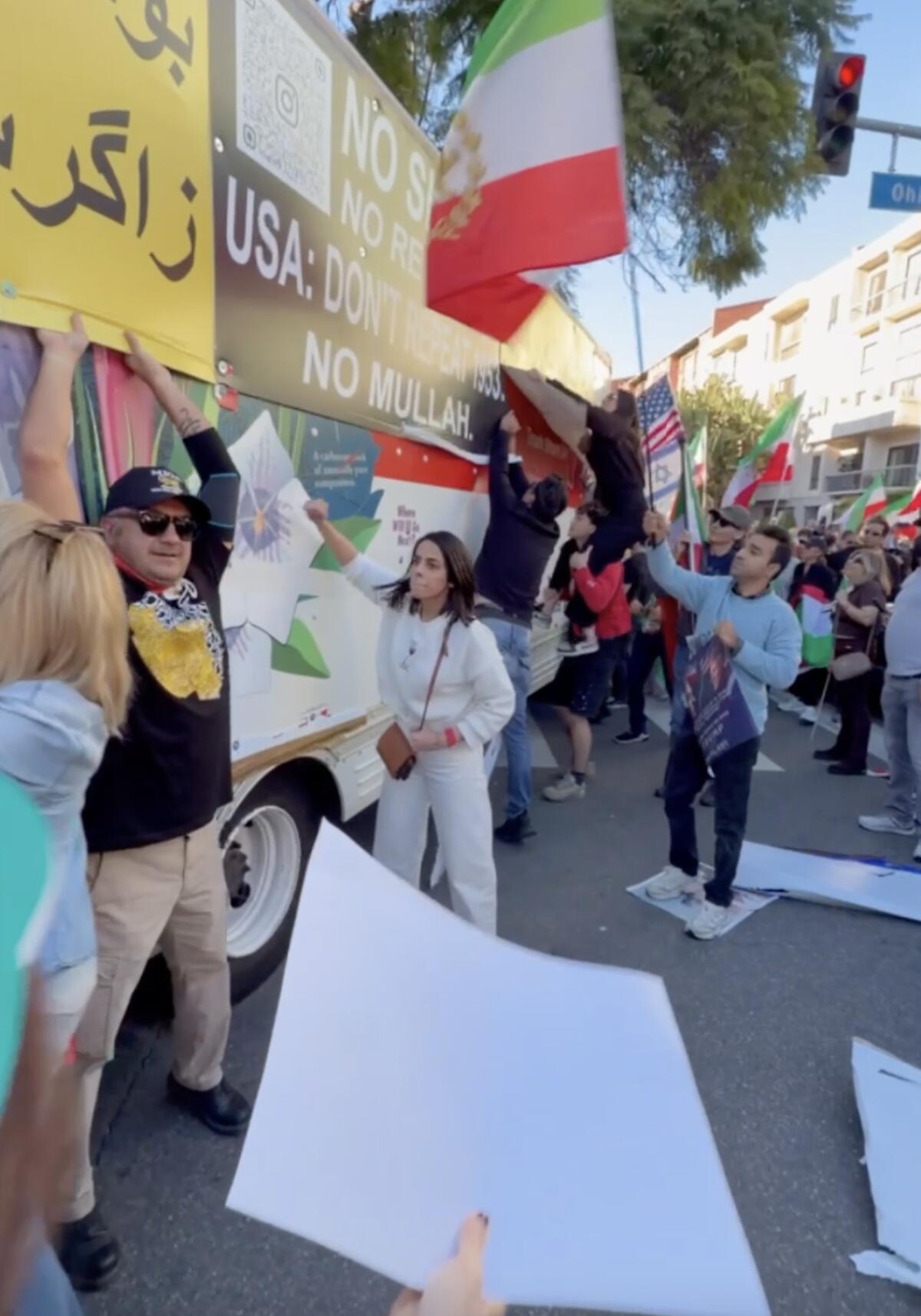 People, some waving green, white and red flags, stand next to a U-Haul truck