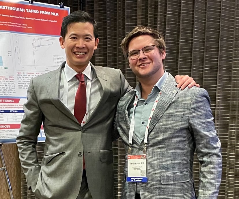 Two men in suits smile for the camera.