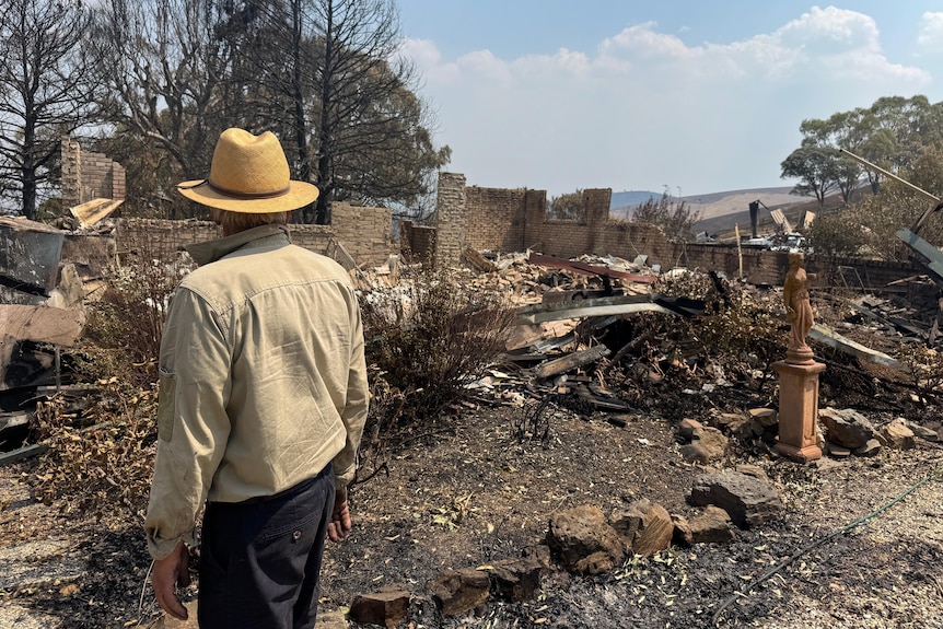 A man looks onto a destroyed and burnt out house.