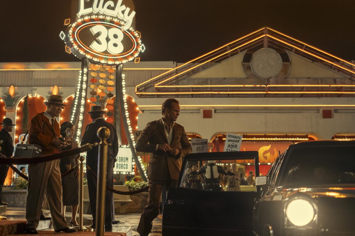 a man steps into of a car near photographers and protestors