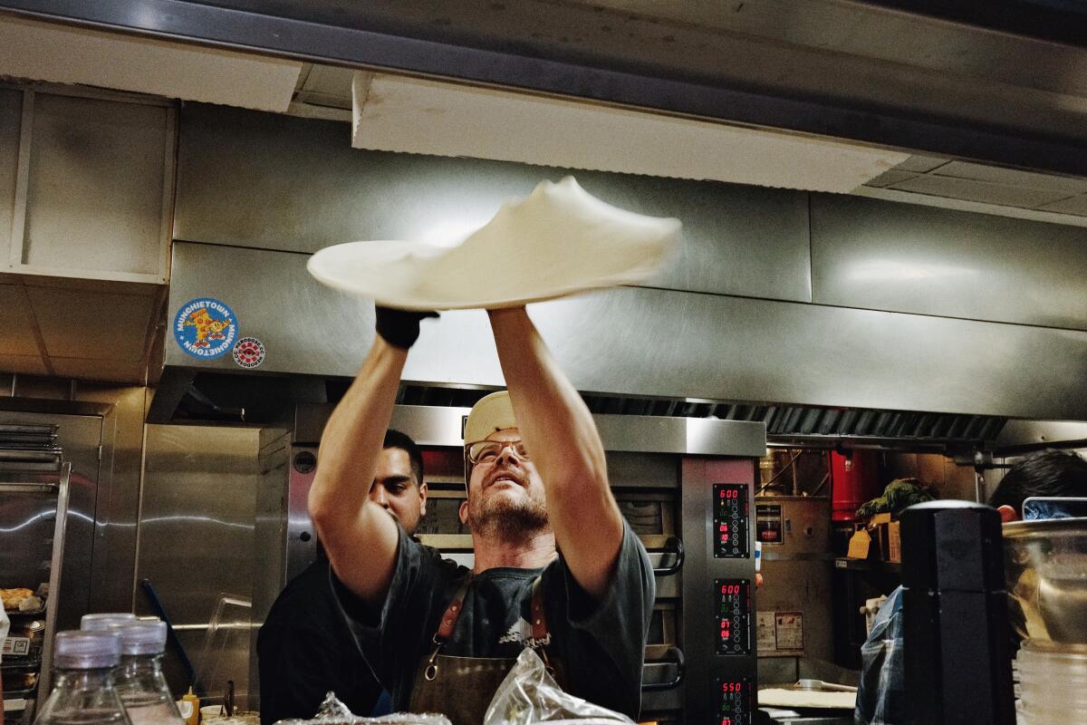 Joe Iverson, of Cliq Claq Pizza, tosses dough into the air in a restaurant kitchen