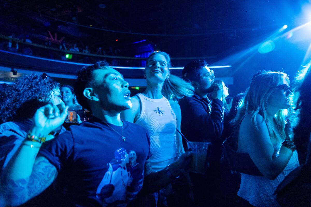 A man with a raised arm stands next to a woman in a white tank top waving her ponytail.