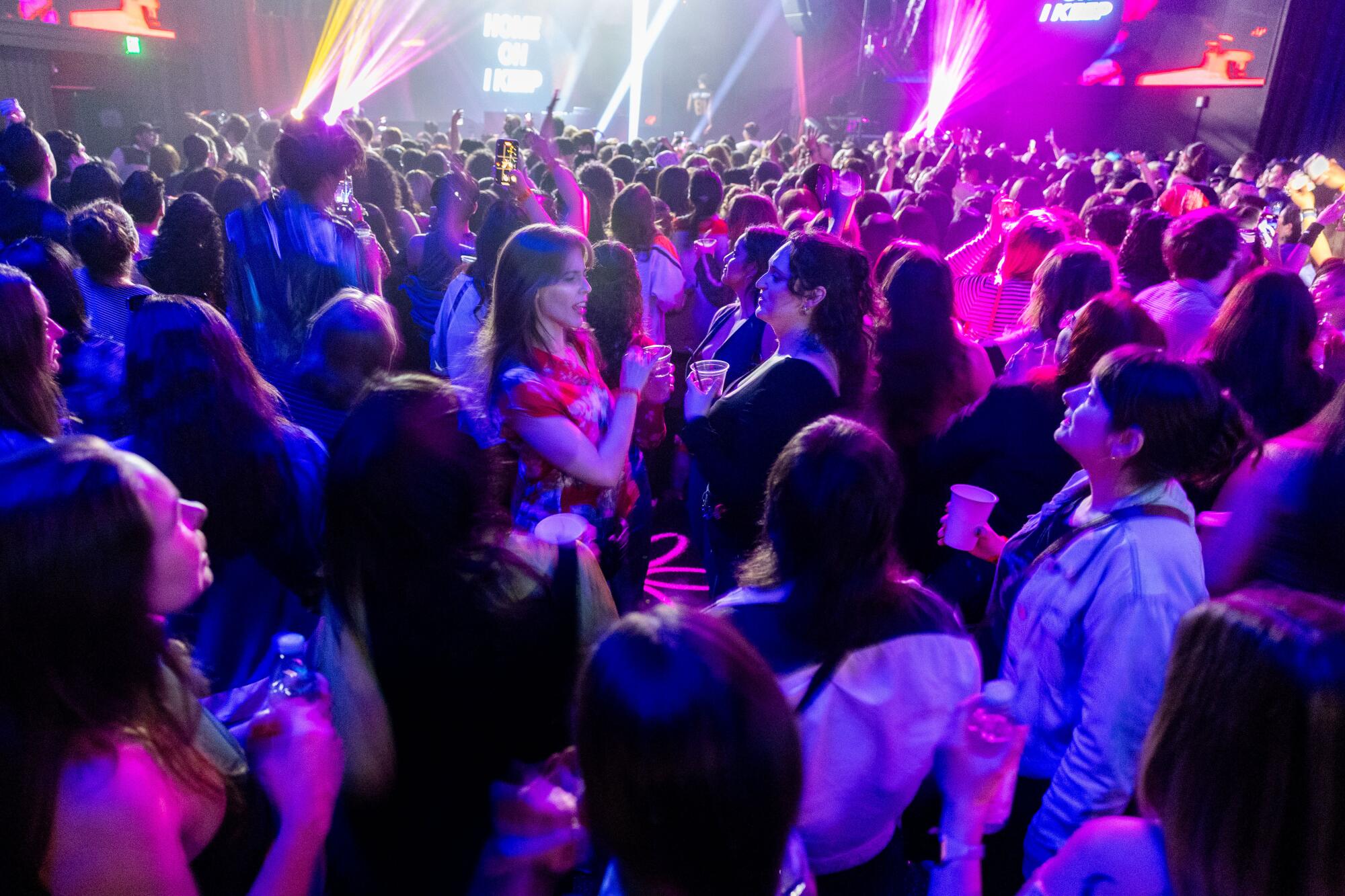 A crowd of people on the dance floor, many holding cups and water bottles.