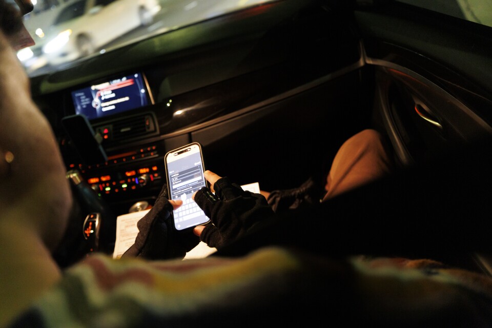 A close up of hands typing on a phone from the passenger's seat of a car at night. 