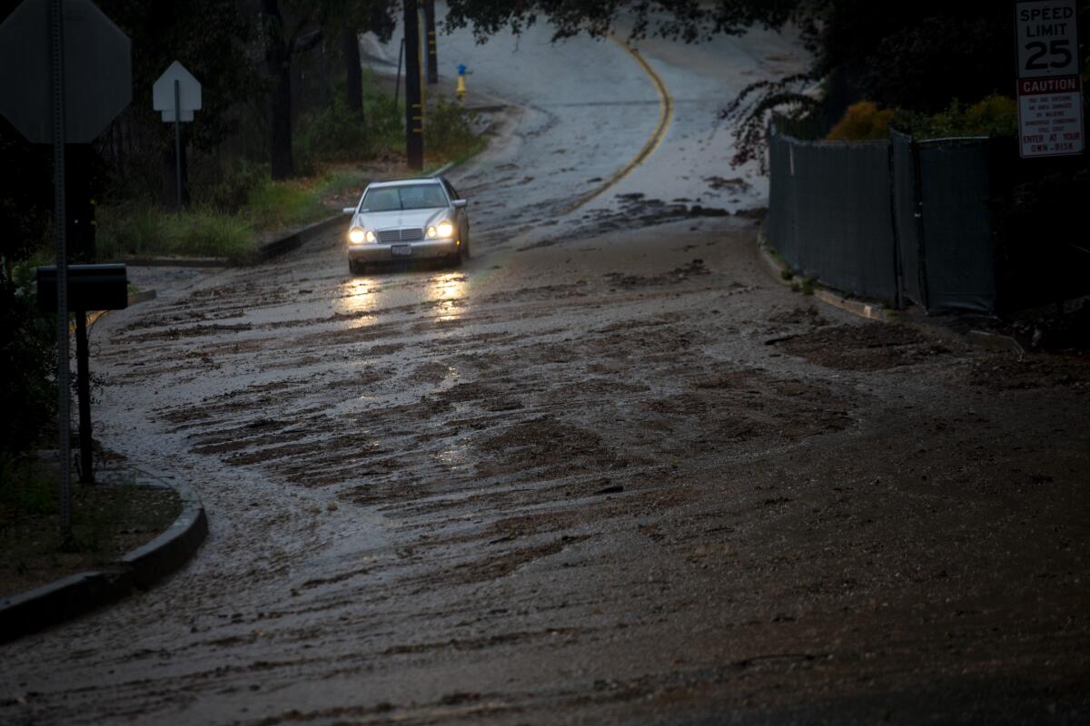A car drives through debris and mud flows on Loma Alta Drive.