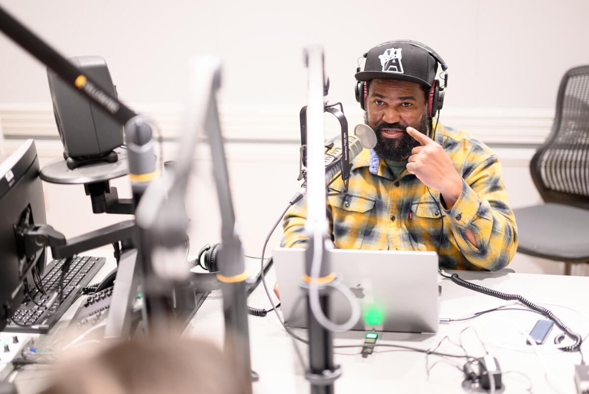 Earlonne Woods in a recording studio speaking into a mic with a laptop at his fingertips. 