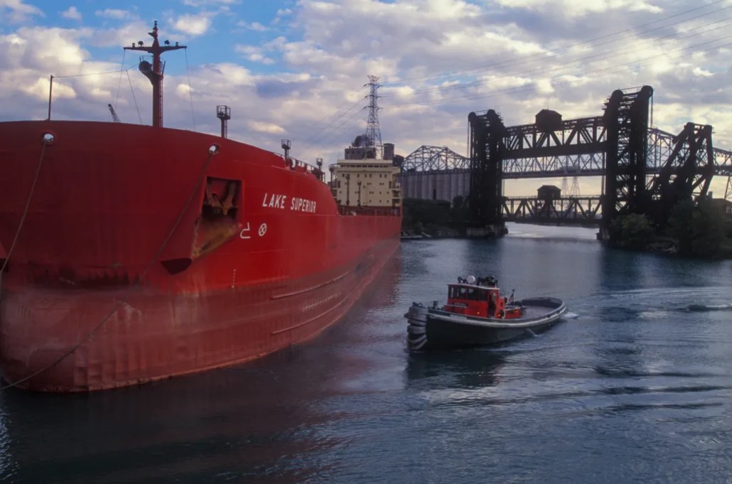 Great Lakes towing tugboat assists freight cargo ship on the mouth of Calumet River in Chicago