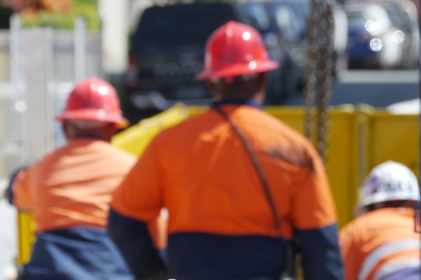 A rear view of construction workers wearing hi-vis safety clothes and hard hats.