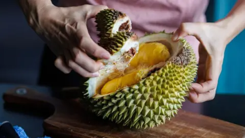 Getty Images Close up of a durian fruit being held in two hands.