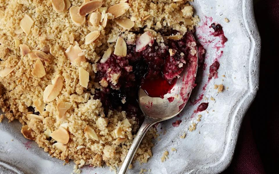 A cherry crumble in white dish sat on wooden table. A spoon sits in the dish.