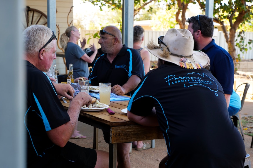 Men and women sit at a pub table eating and drinking. One wears a wide-brimmed hat and Farmers Across Borders uniform.