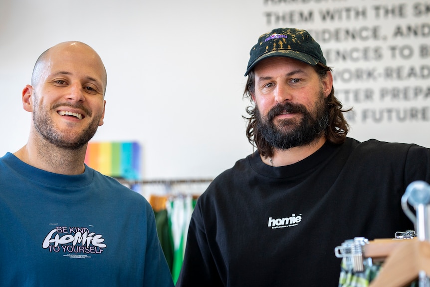 Nick Pearce and Marcus Crook stand next to a rack of clothing. 