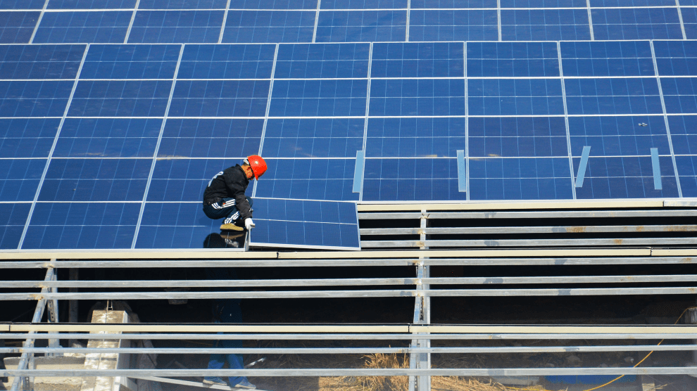 A man dressed in black wearing a red hard hat crouches as he lowers one of dozens of panels into place.