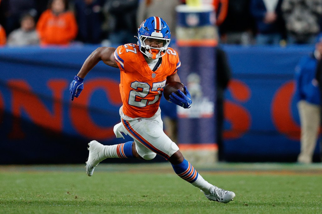 A Denver Broncos player in an orange jersey and blue helmet running with the football.