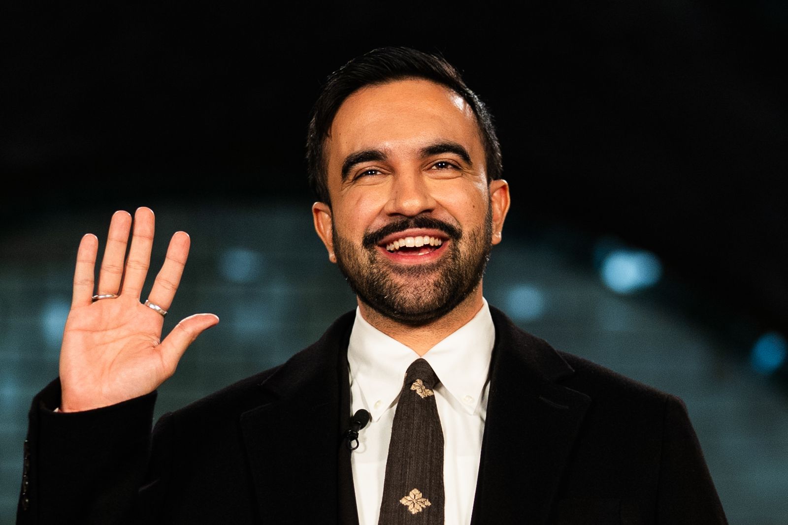 Image may contain Head Person Face Happy Smile Dimples Adult Clothing Coat Accessories Formal Wear and Tie