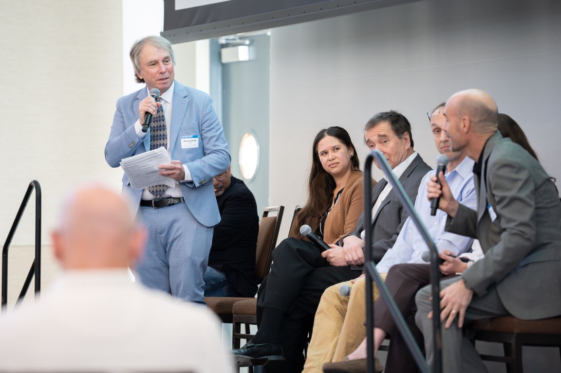 A panel of seated researchers engage in discussion with UCLA's Michael Jerrett who stands with a microphone. 