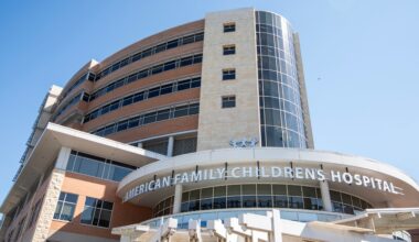 A modern multi-story building with glass and stone features, displaying the sign American Family Childrens Hospital under a clear blue sky.