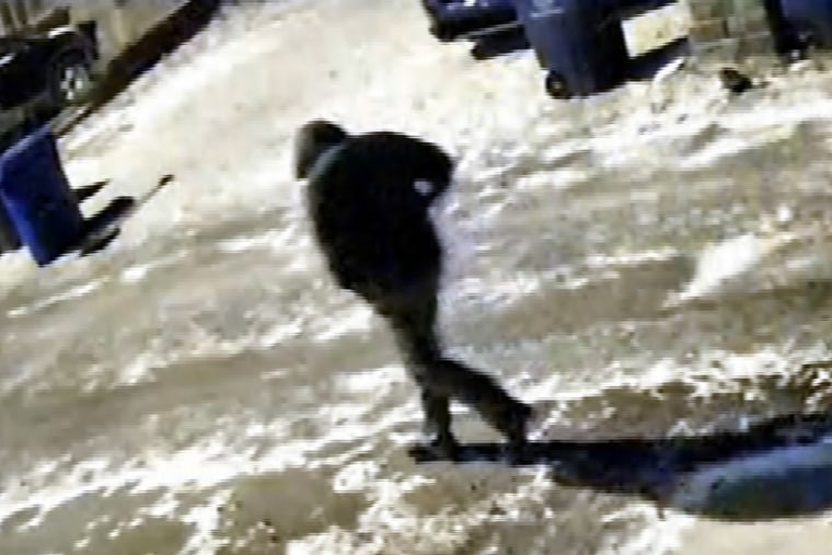 A person walks outside on a residential street, snowy street, person wearing dark clothing and hood