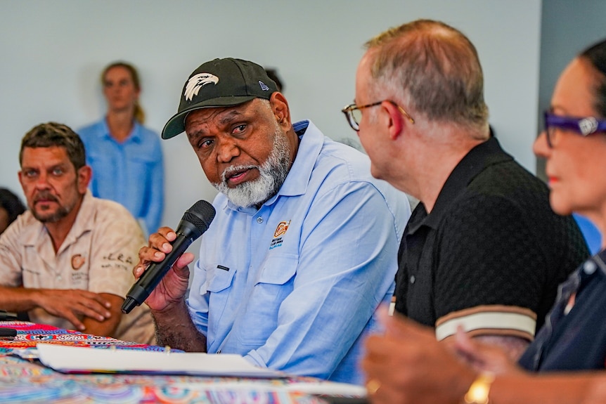 an Indigenous man with a microphone speaking to another man.