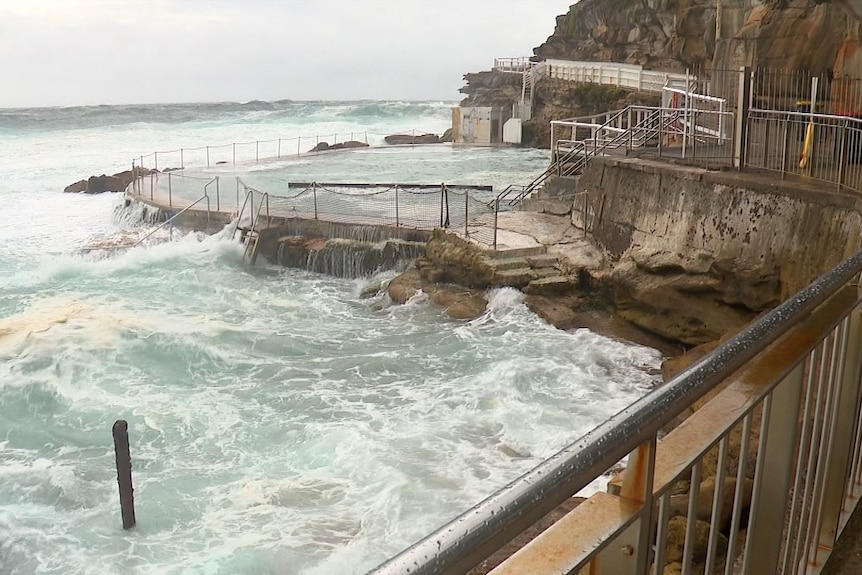 Choppy dark waves crash against a rock pool at a Sydney beach.
