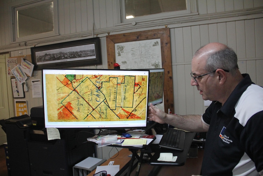 A man with glasses refers to a yellow map on a screen. 