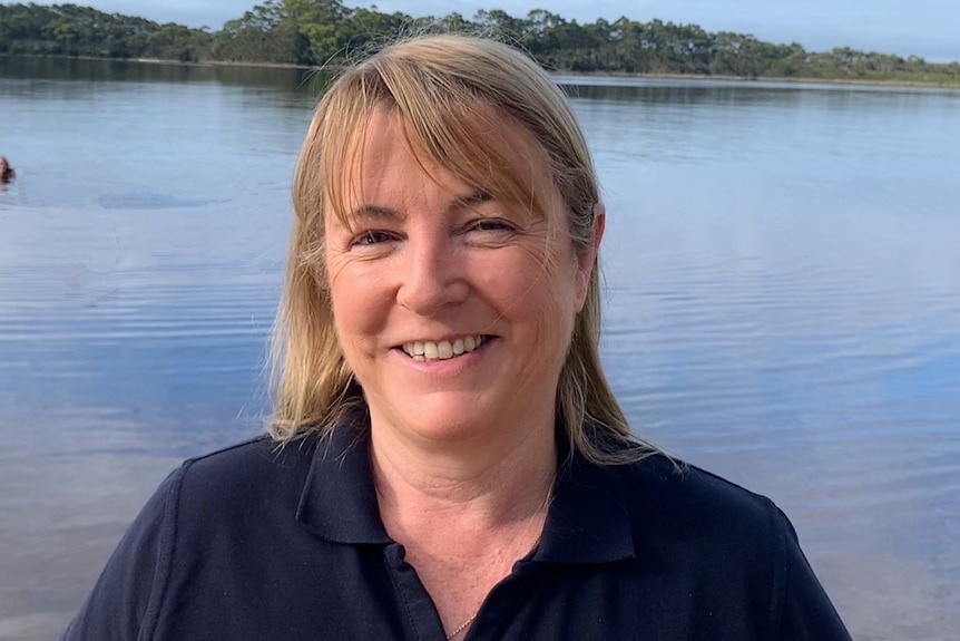 A blond woman in front of a body of water