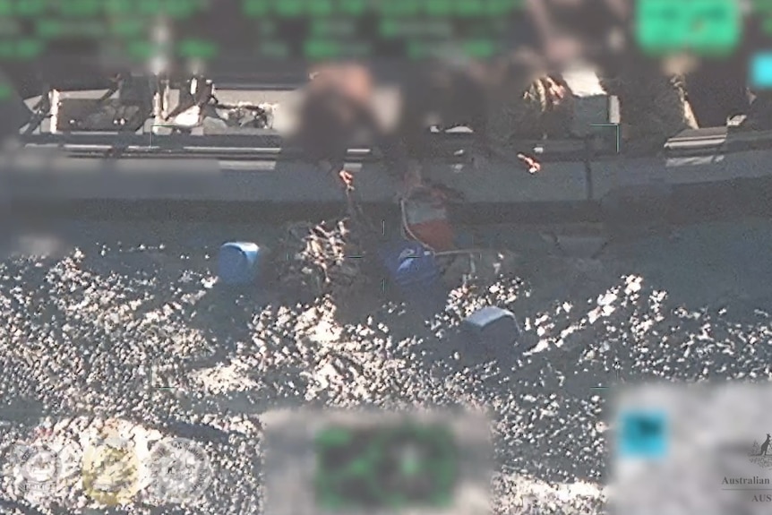 Digitally blurred people leaning over the side of a rubber dinghy collecting bags from the ocean.