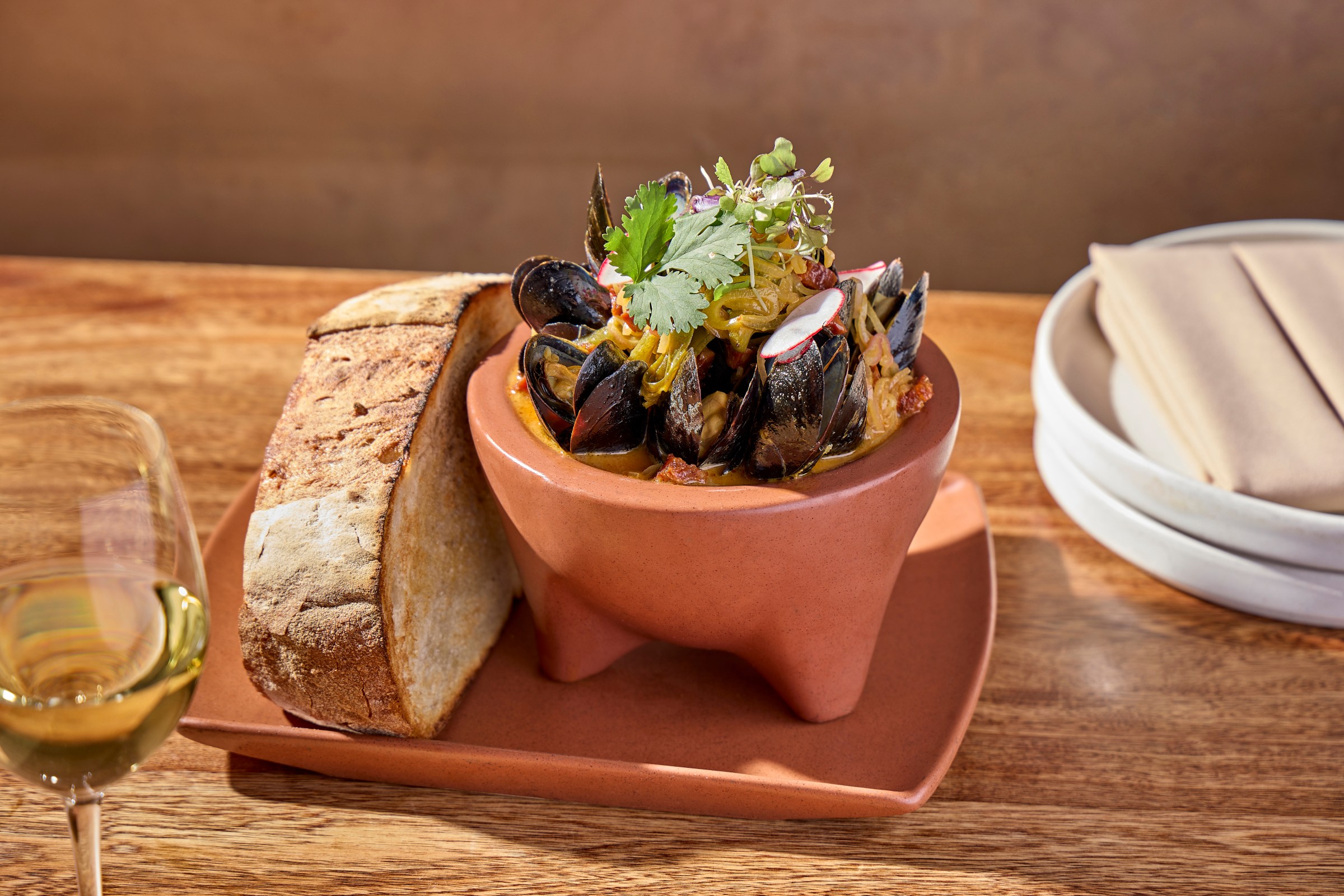 A pile of mussels in a stone bowl with a slice of bread.