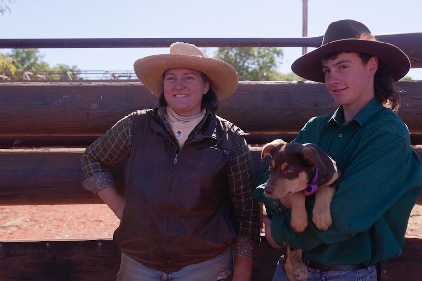 A woman stands next to a teenage boy who is holding a Kelpie puppy,