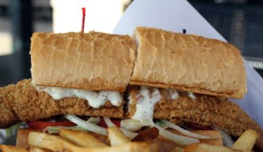 Fried catfish po’ boy ($14.95) is dressed with lettuce, tomatoes, onion, pickles and tartar sauce, and served with fries and two hush puppies. (Karen Chaney/Community Impact)
