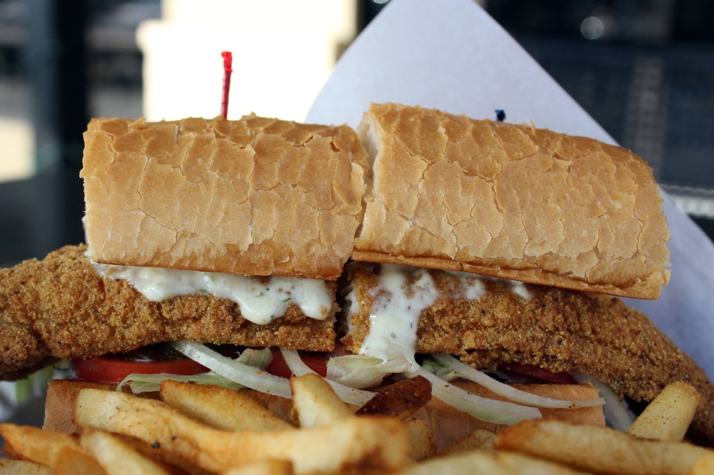Fried catfish po’ boy ($14.95) is dressed with lettuce, tomatoes, onion, pickles and tartar sauce, and served with fries and two hush puppies. (Karen Chaney/Community Impact)
