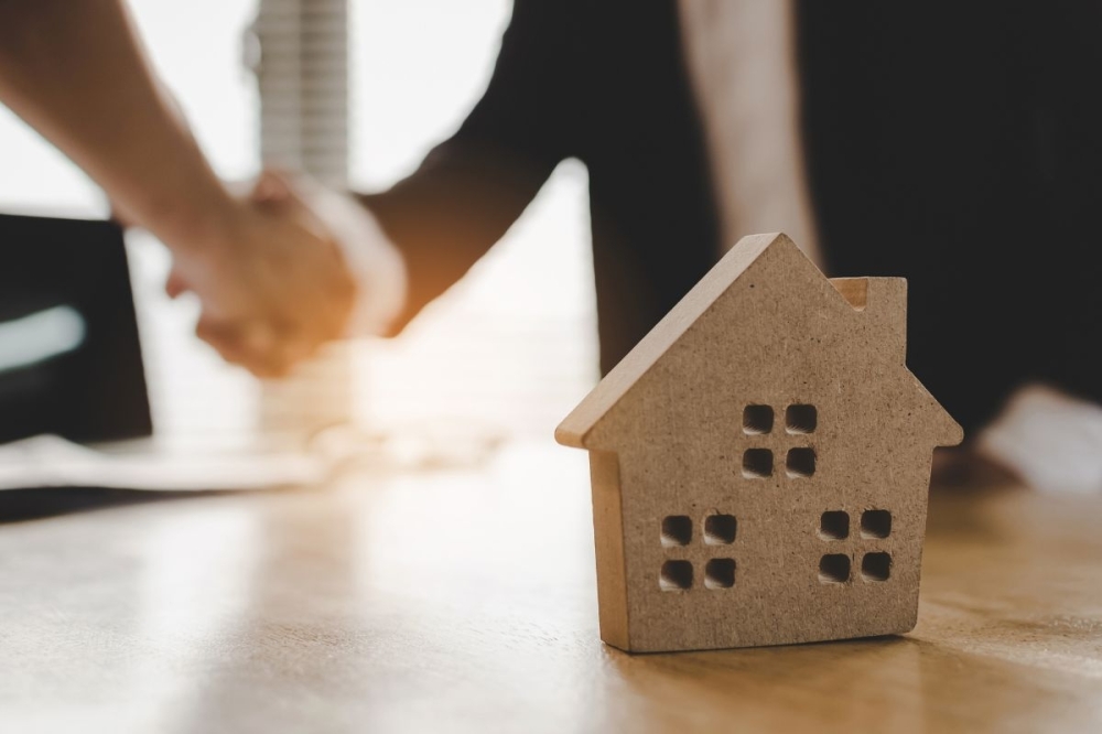 Realtors shake hands in front of a house mold.