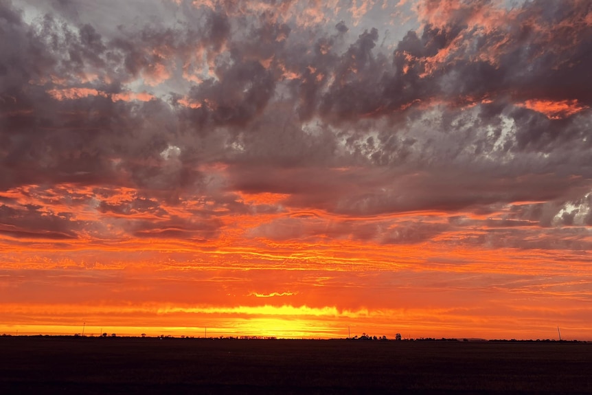 Dark horizon with orange sky and grey clouds above it.