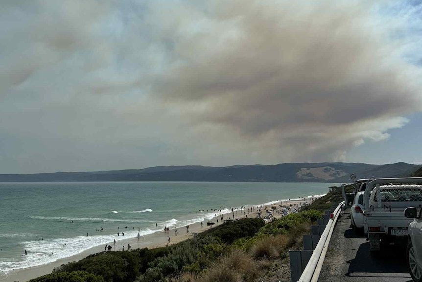 Smoke from a bushfire can be seen in the distance from a beach.