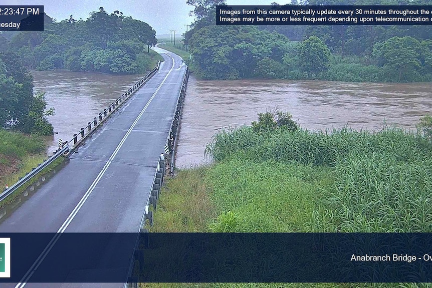 A swollen river rises almost to the level of a causeway in a country area.