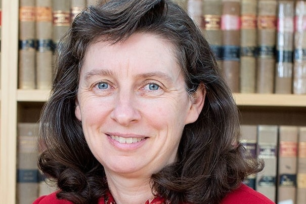 Woman with dark brown hair, blue eyes, books behind her, close up shot