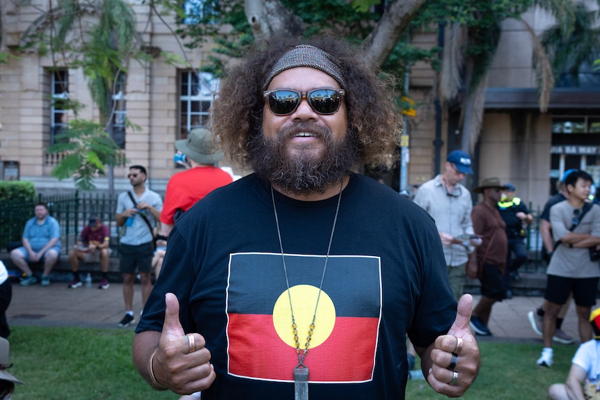 A man smiles wearing a black shirt with the Aboriginal flag on it.