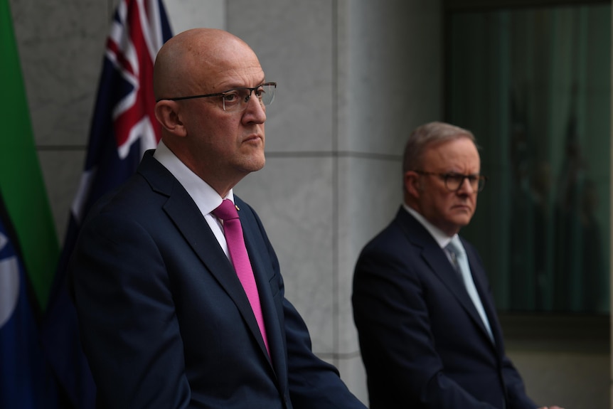 Men in suits standing in a press conference.