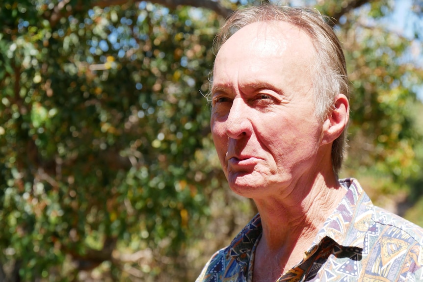 A man standing in front of trees and looking to the side