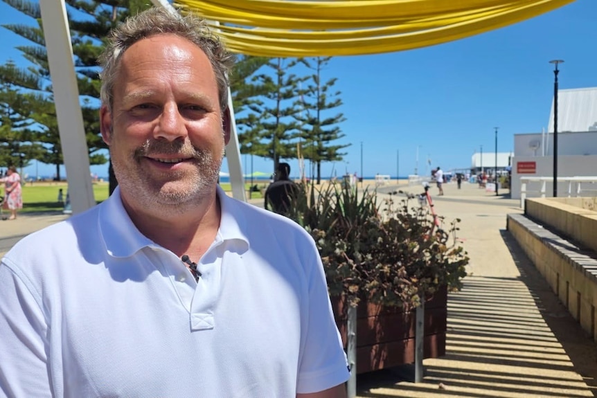 A man in a white polo shirt stands on the Busselton foreshore
