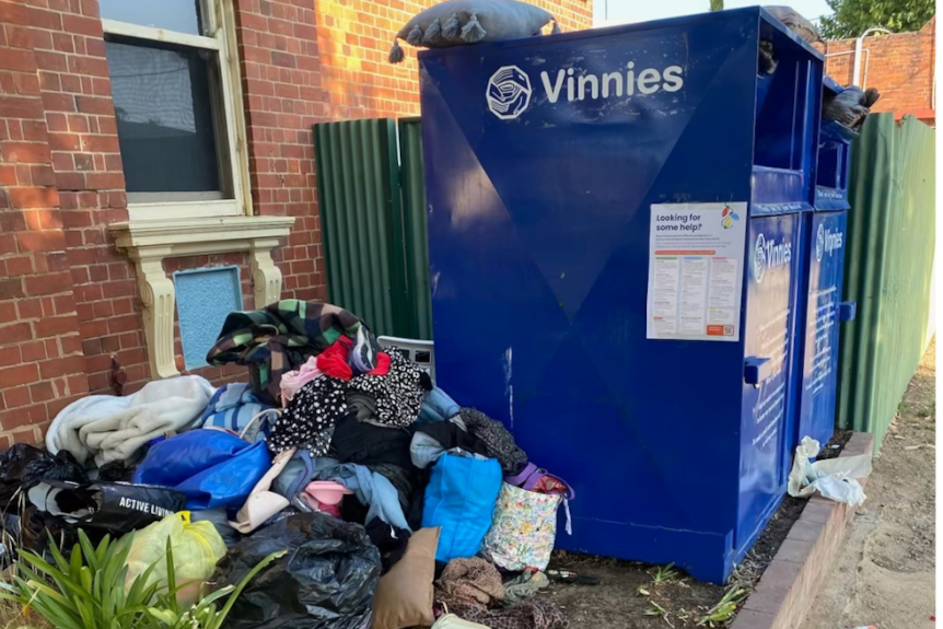A blue St Vincent's donation bin with overflowing bags of donations on the ground and in the bin.