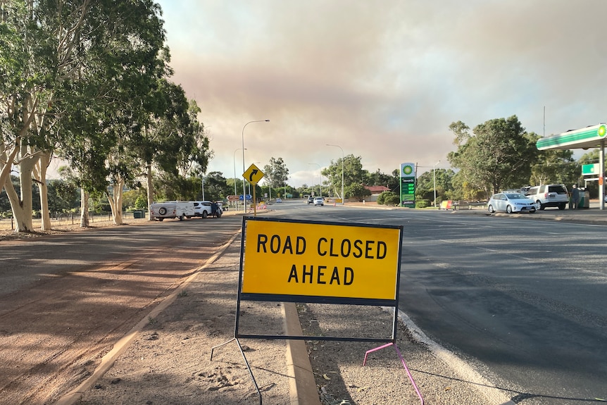 Smoke in the sky, road closure sign on the ground