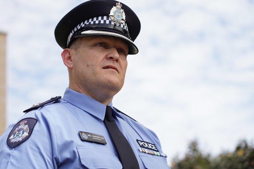 A police officer in uniform stands outside a police station. 