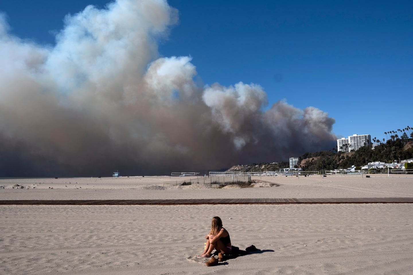 A lone sunbather sat and watched a large plume of smoke from a wildfire rise over the Pacific Palisades, in Santa Monica, Calif., on Jan. 7.