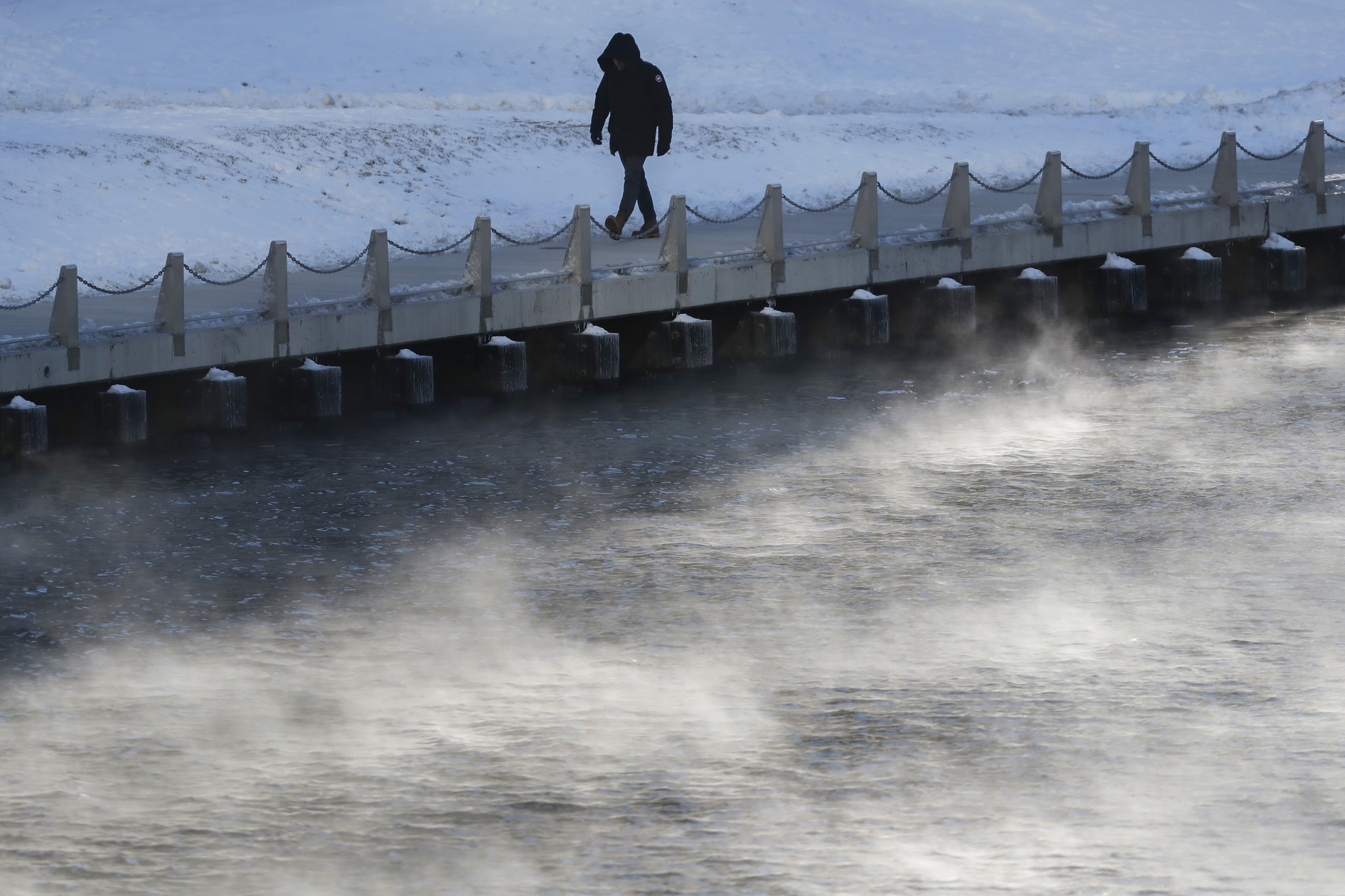 A man walks along the Chicago Riverwalk on a cold...