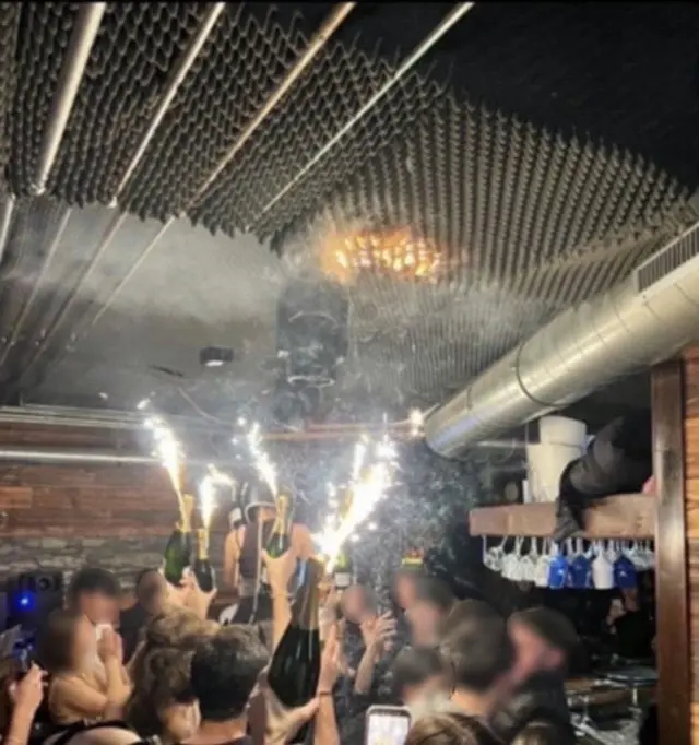 People holding champagne bottles with sparklers attached in the Swiss nightclub - flames can be seen in the ceiling