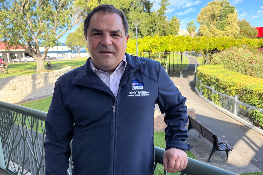 A man with a Liberal logo on his jacket standing in front of a garden