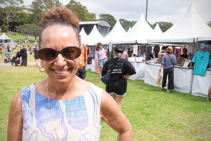 A woman in sunglasses smiling at the camera at a festival