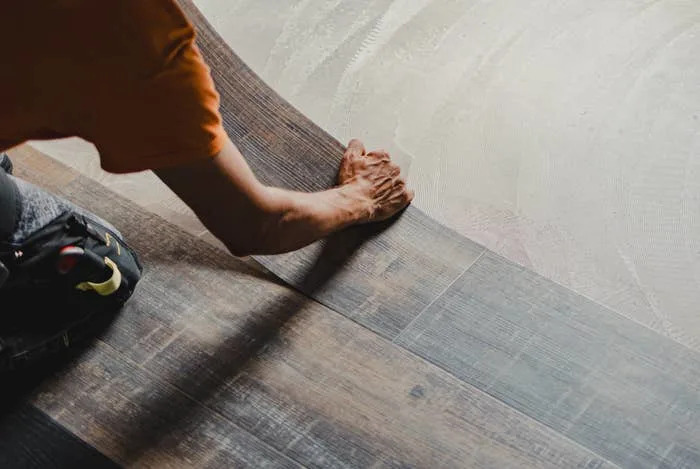 Person installing wood-like vinyl flooring, smoothing it with their hand